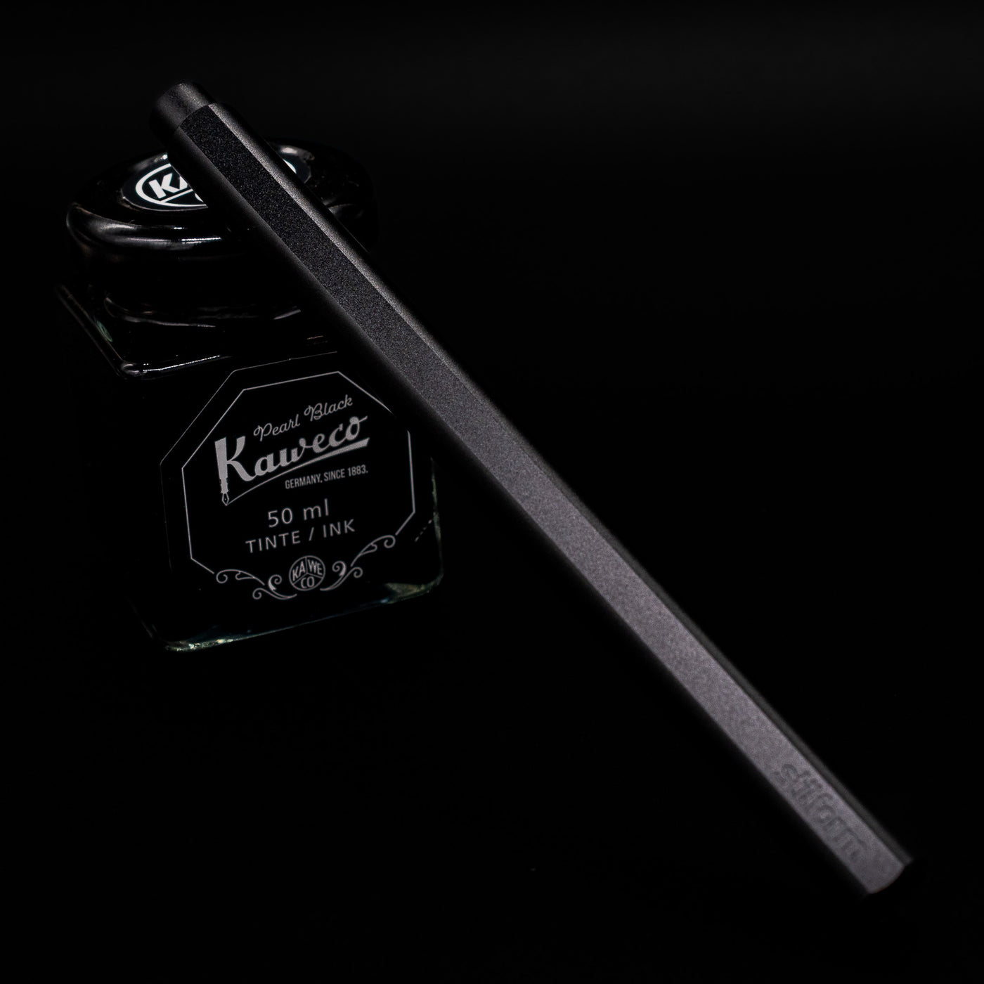 Stilform FLOW Rollerball Pen – Warp Black Aluminum leaning on an ink bottle capped.