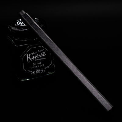 Stilform FLOW Rollerball Pen – Warp Black Aluminum leaning on an ink bottle capped.