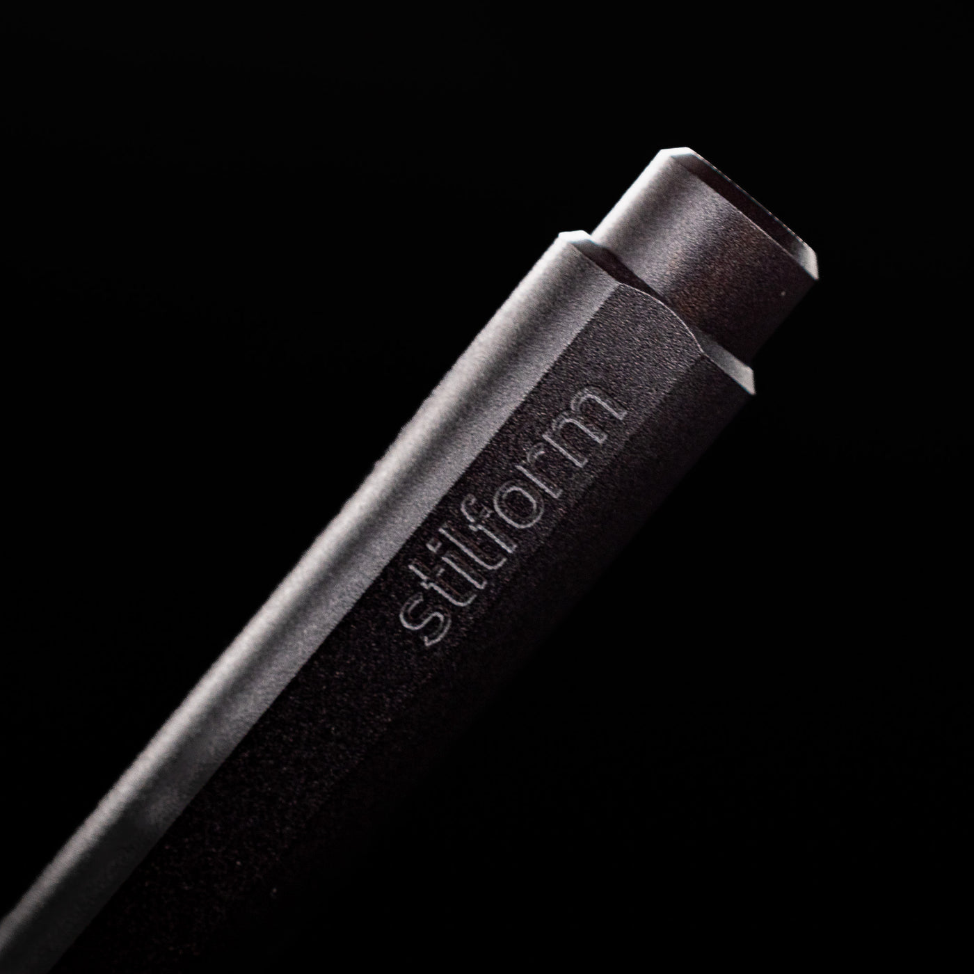 A macro shot of the logo at the bottom of the Stilform FLOW Rollerball Pen – Warp Black Aluminum posted.