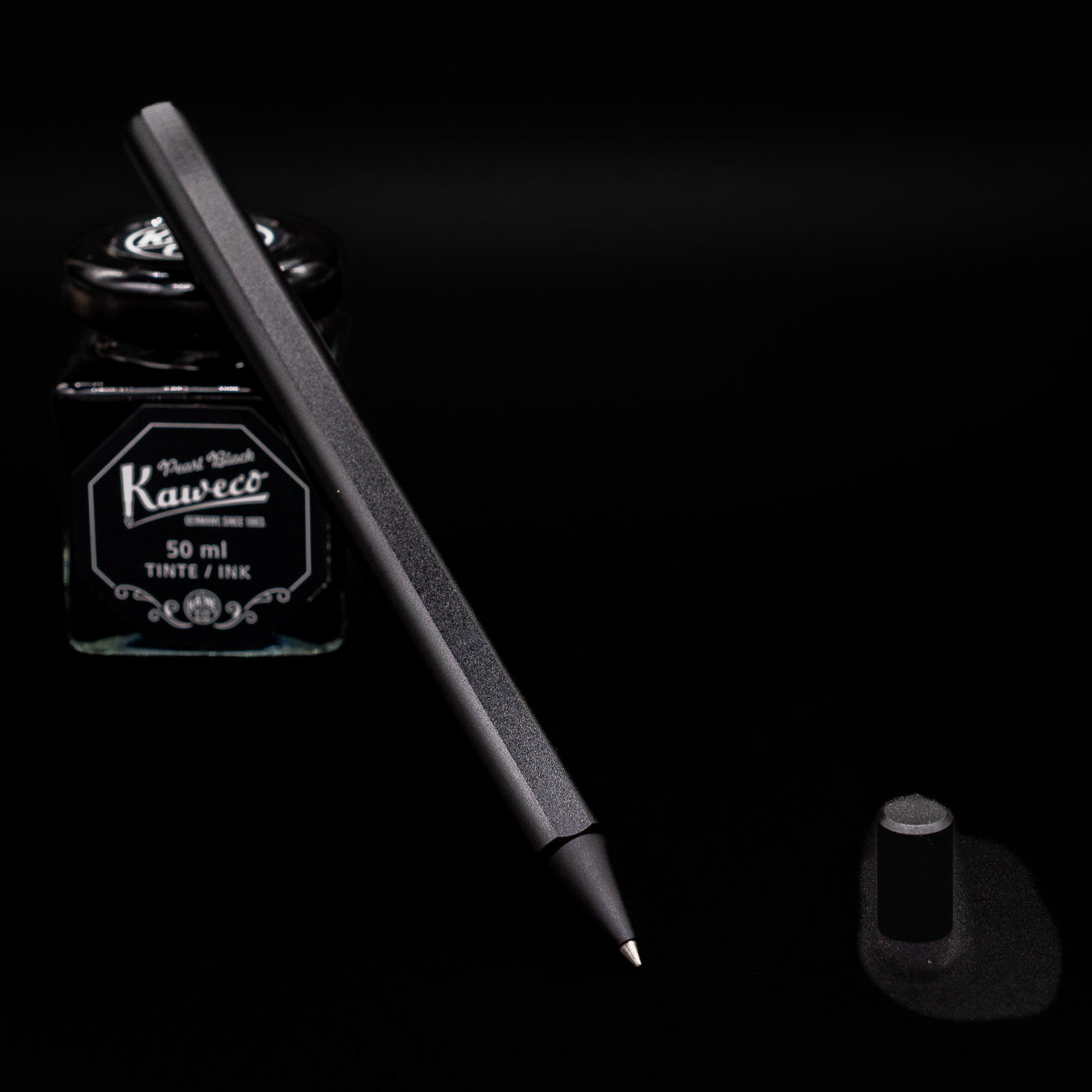 Stilform FLOW Rollerball Pen – Warp Black Aluminum uncapped leaning on an ink bottle.