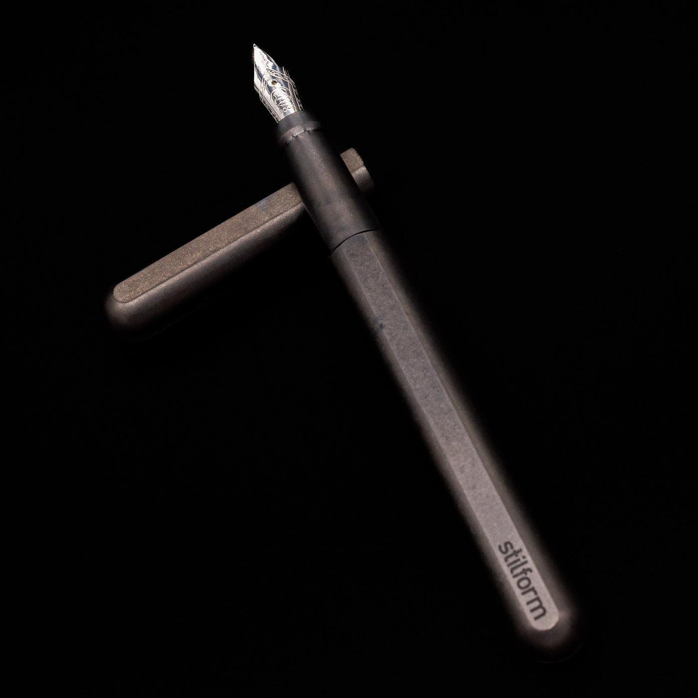 Stilform INK Fountain Pen – Titanium DLC laying on top of its cap in a crossed position showing full view of the entire uncapped pen.