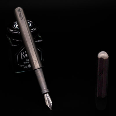 Stilform INK Fountain Pen – Titanium DLC leaning on an ink bottle uncapped showcasing the detailing on the nib.