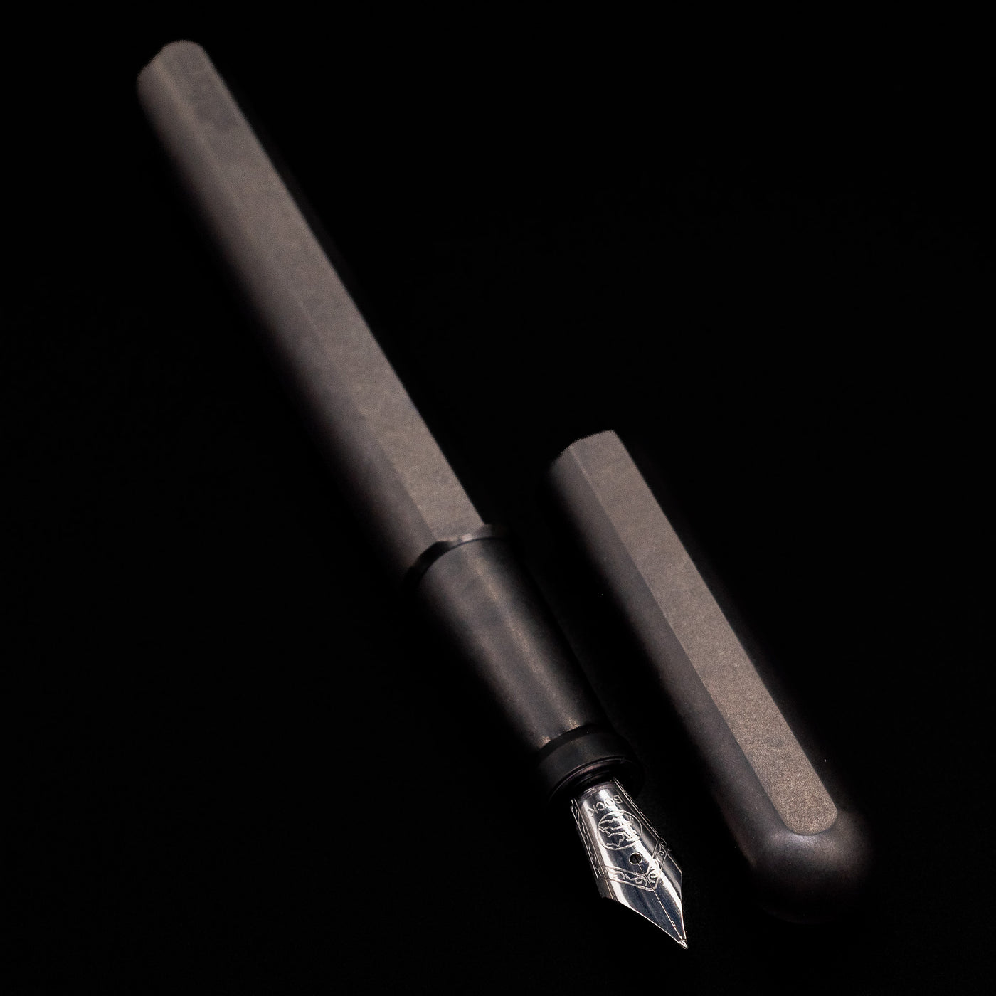 A full view of the Stilform INK Fountain Pen – Titanium DLC uncapped, with its cap laying next to the pen. 