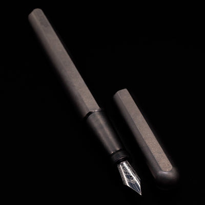 A full view of the Stilform INK Fountain Pen – Titanium DLC uncapped, with its cap laying next to the pen. 