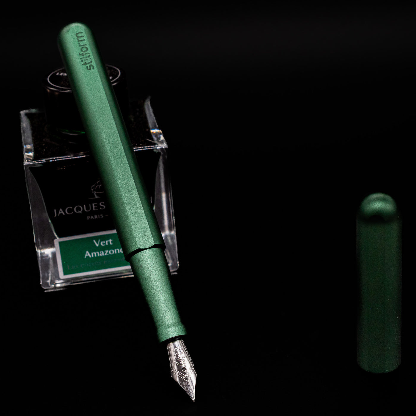 Stilform INK Fountain Pen – Aurora Green Aluminum leaning on an ink bottle uncapped showcasing the detailing on the nib.