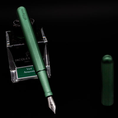 Stilform INK Fountain Pen – Aurora Green Aluminum leaning on an ink bottle uncapped showcasing the detailing on the nib.