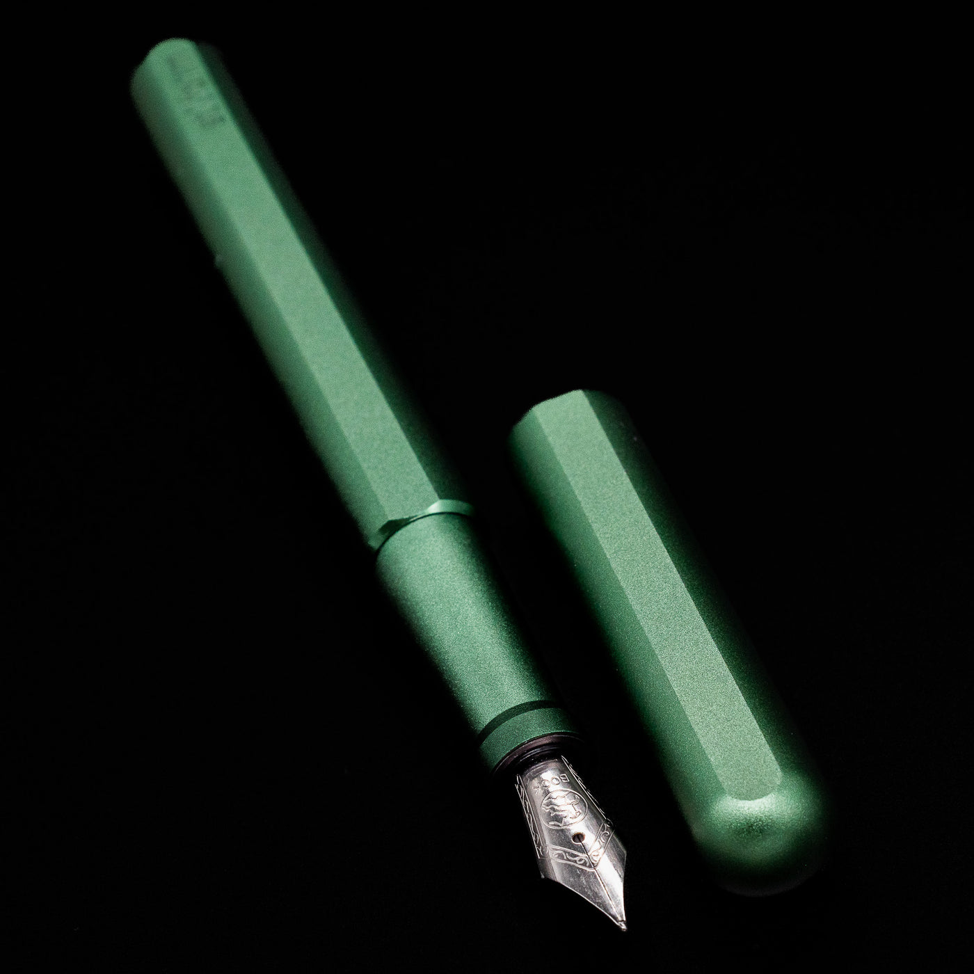  A full view of the Stilform INK Fountain Pen – Aurora Green Aluminum uncapped, with its cap laying next to the pen. 