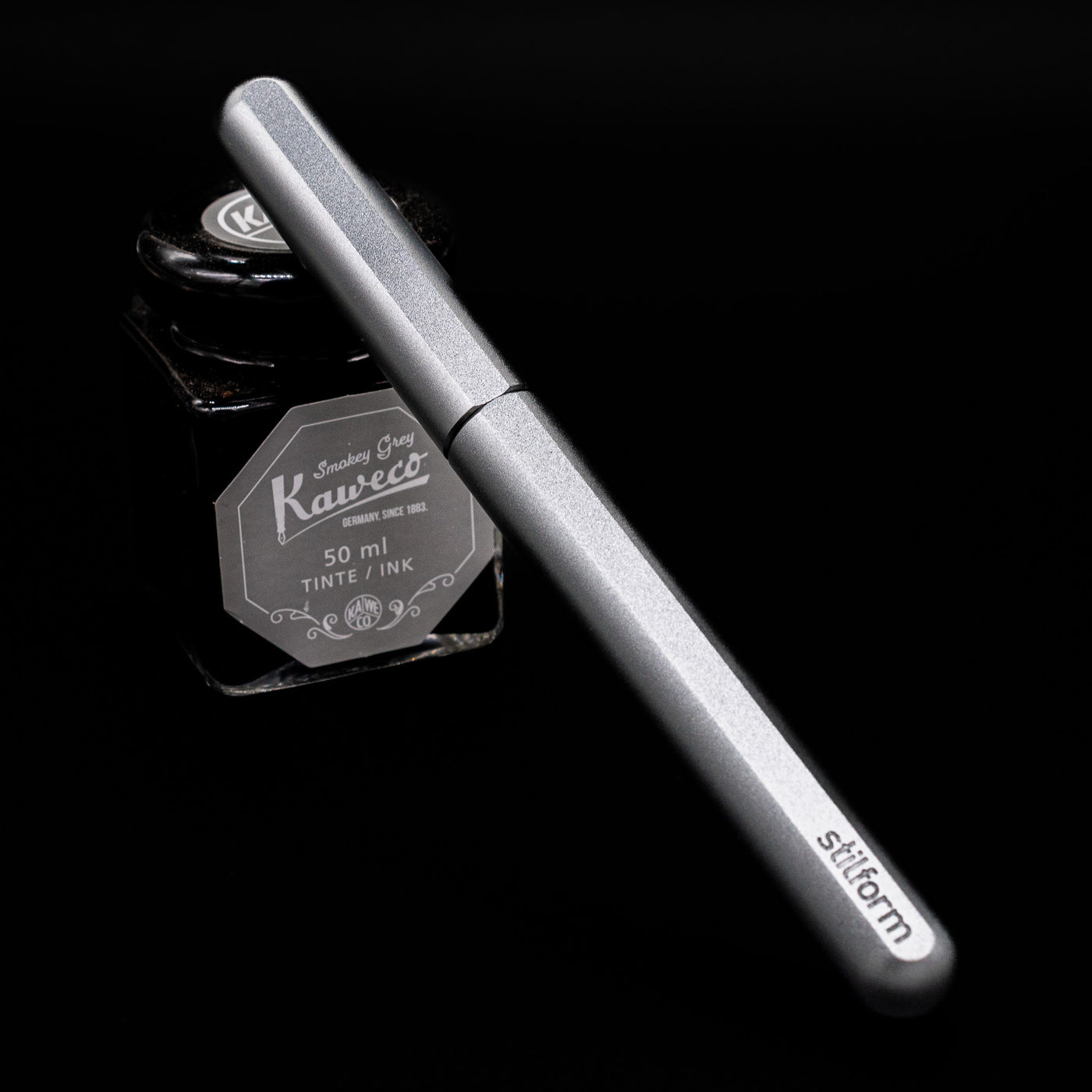 Stilform INK Fountain Pen – Comet Grey Aluminum capped, leaning against an ink bottle. 