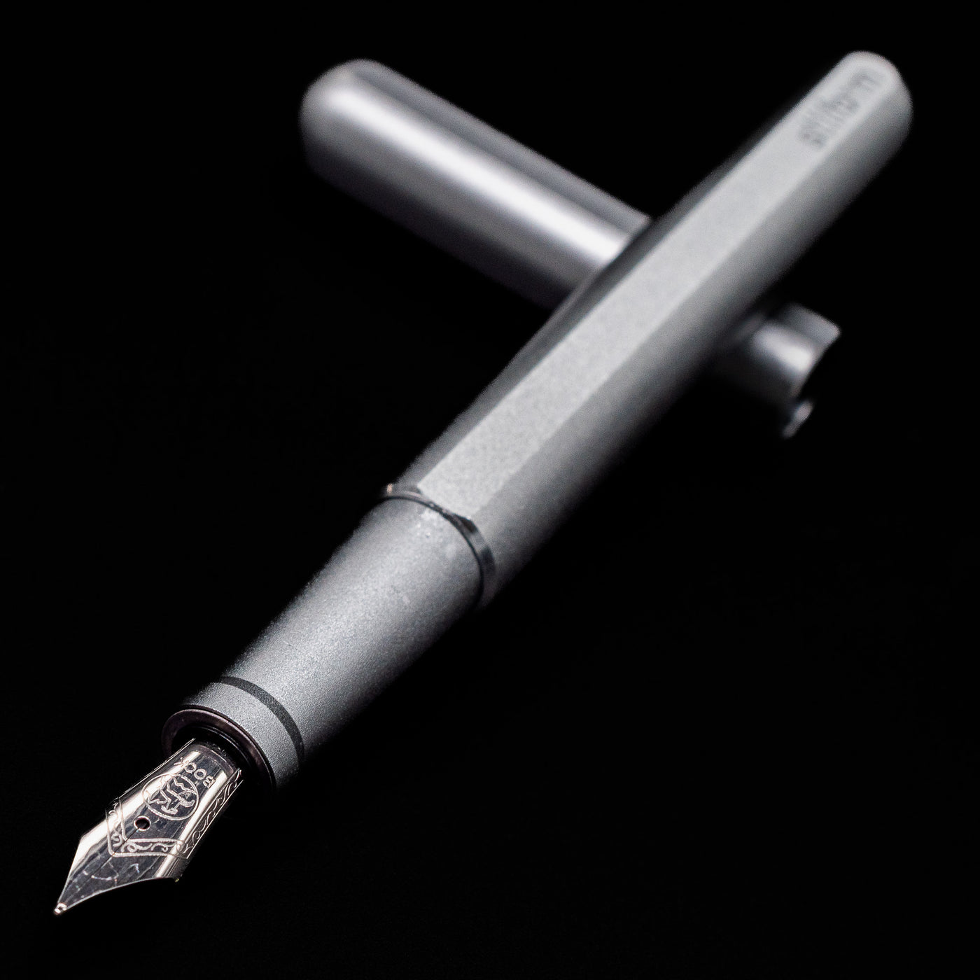 Stilform INK Fountain Pen – Comet Grey Aluminum laying across its own cap, crossed, with a focus on the nib.