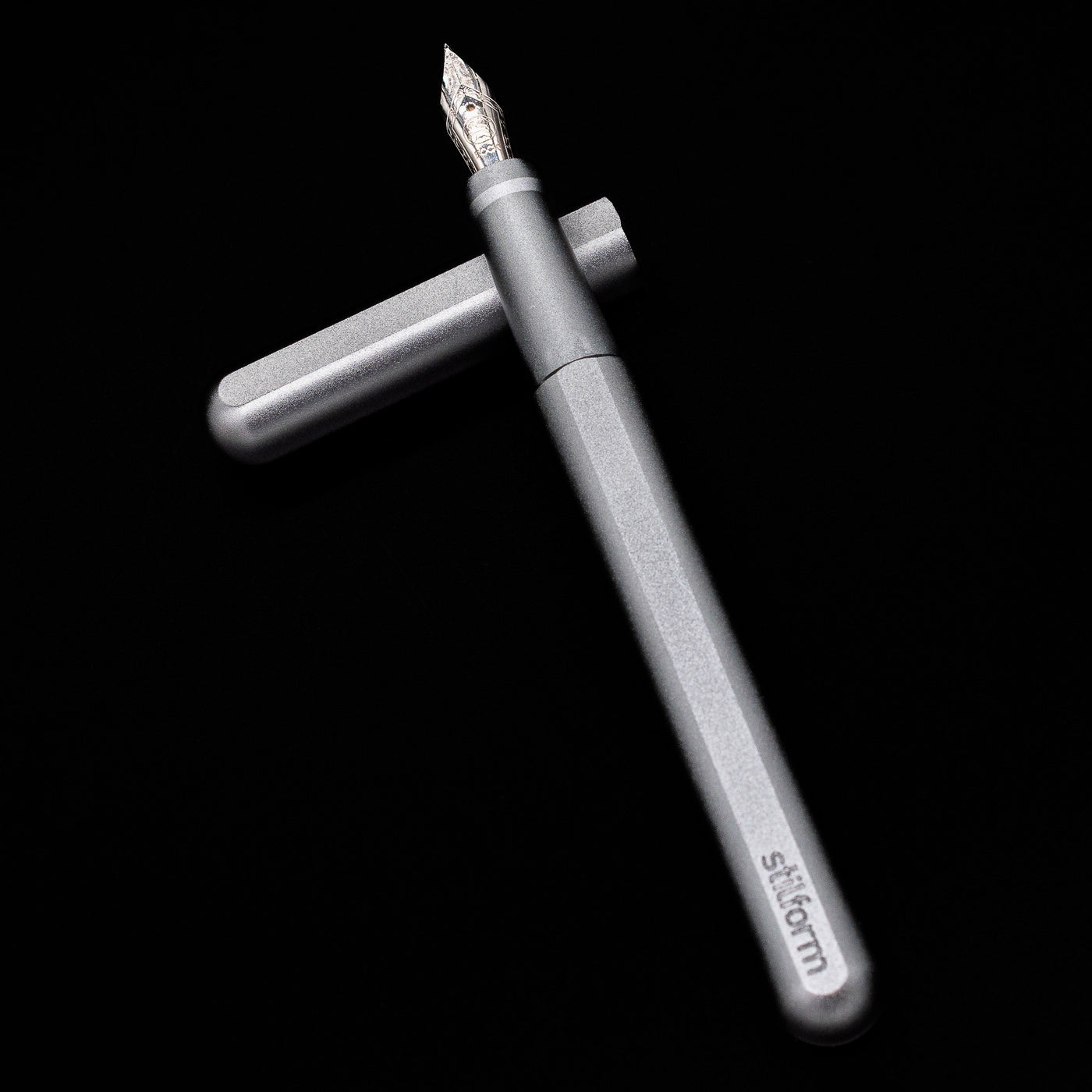 Stilform INK Fountain Pen – Comet Grey Aluminum laying on top of its cap in a crossed position showing full view of the entire uncapped pen.