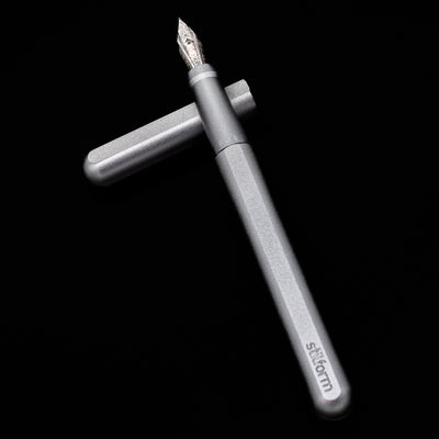 Stilform INK Fountain Pen – Comet Grey Aluminum laying on top of its cap in a crossed position showing full view of the entire uncapped pen.