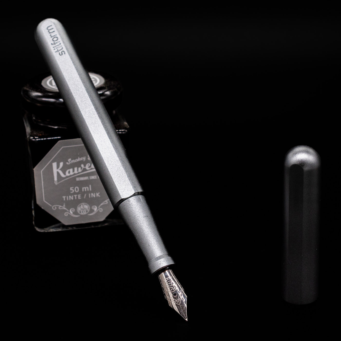 Stilform INK Fountain Pen – Comet Grey Aluminum leaning on an ink bottle uncapped showcasing the detailing on the nib.