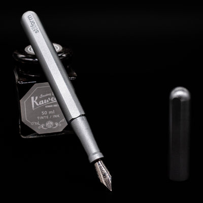 Stilform INK Fountain Pen – Comet Grey Aluminum leaning on an ink bottle uncapped showcasing the detailing on the nib.
