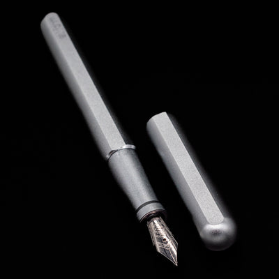 A full view of the Stilform INK Fountain Pen – Comet Grey Aluminum uncapped, with its cap laying next to the pen. 