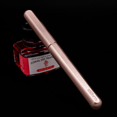 Stilform INK Fountain Pen – Rose Moon Aluminum capped, leaning against an ink bottle.
