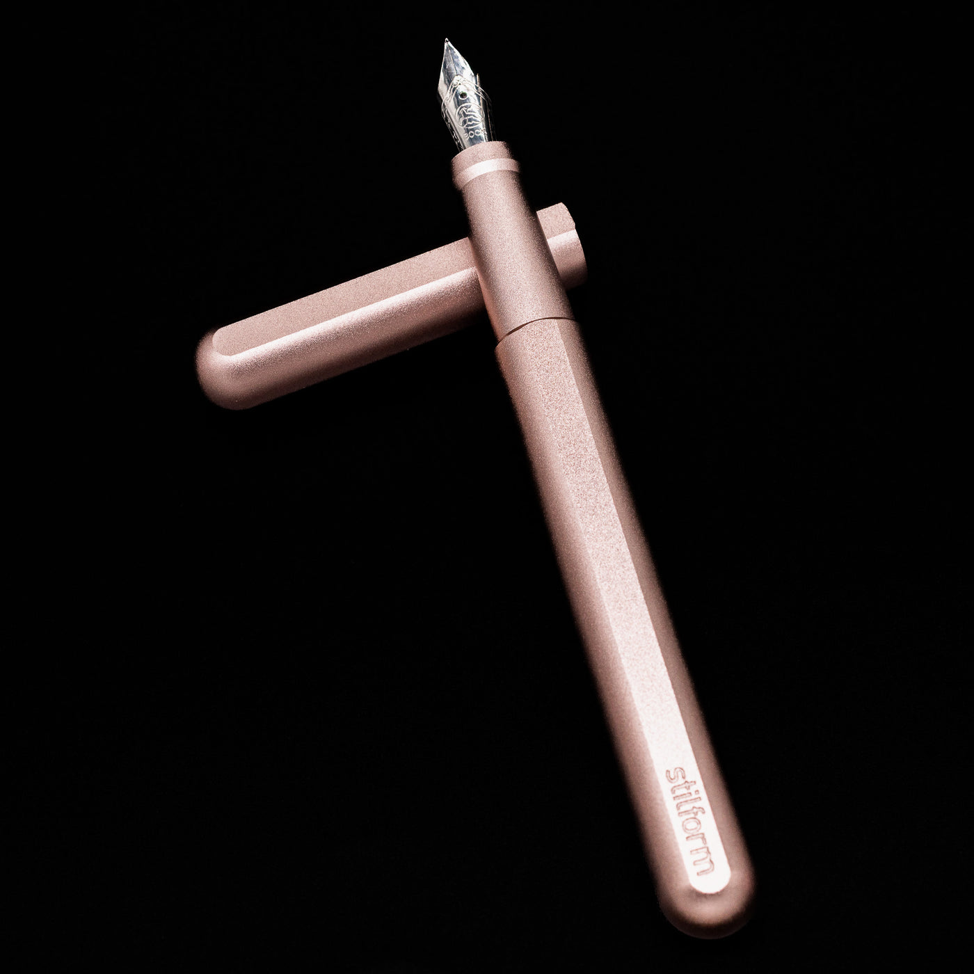Stilform INK Fountain Pen – Rose Moon Aluminum laying on top of its cap in a crossed position showing full view of the entire uncapped pen.
