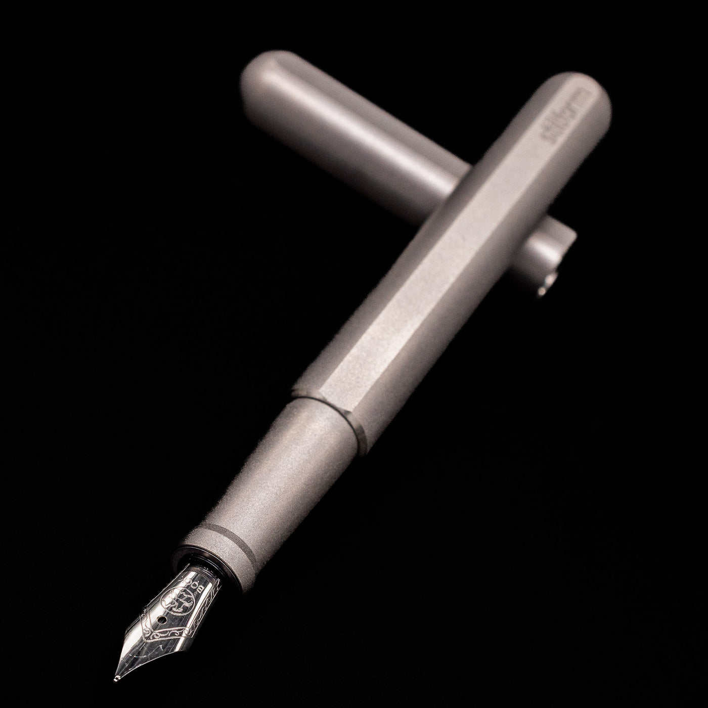 Stilform INK Fountain Pen – Titanium Matte laying across its own cap, crossed, with a focus on the nib.