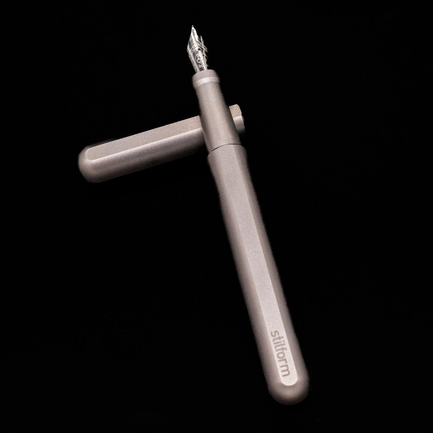 Stilform INK Fountain Pen – Titanium Matte laying on top of its cap in a crossed position showing full view of the entire uncapped pen.