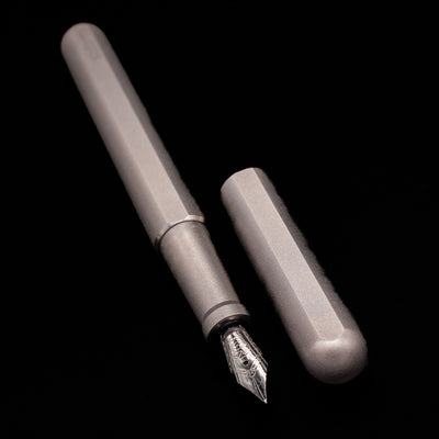 A full view of the Stilform INK Fountain Pen – Titanium Matte uncapped, with its cap laying next to the pen. 