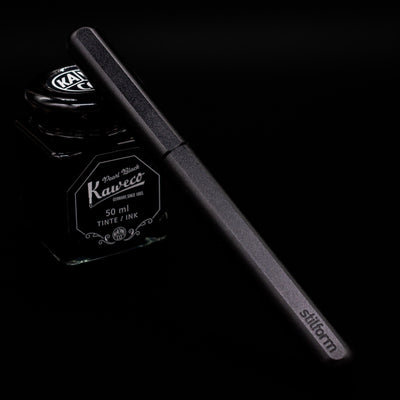 Stilform INK Fountain Pen – Warp Black Aluminum capped, leaning against an ink bottle. 