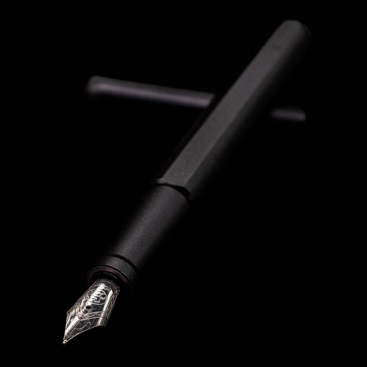 Stilform INK Fountain Pen – Warp Black Aluminum laying across its own cap, crossed, with a focus on the nib.