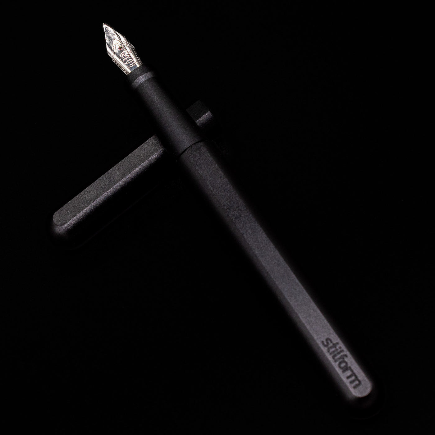 Stilform INK Fountain Pen – Warp Black Aluminum laying on top of its cap in a crossed position showing full view of the entire uncapped pen.