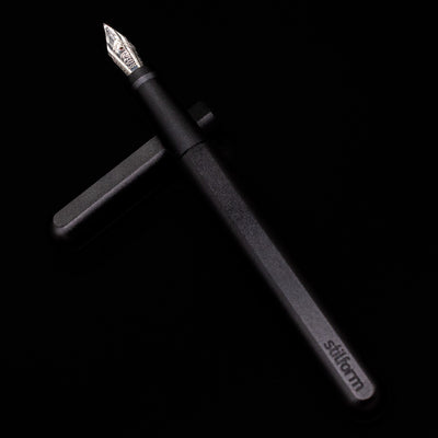 Stilform INK Fountain Pen – Warp Black Aluminum laying on top of its cap in a crossed position showing full view of the entire uncapped pen.