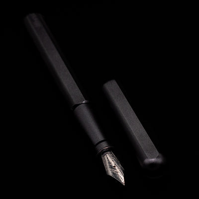  A full view of the Stilform INK Fountain Pen – Warp Black Aluminum uncapped, with its cap laying next to the pen. 