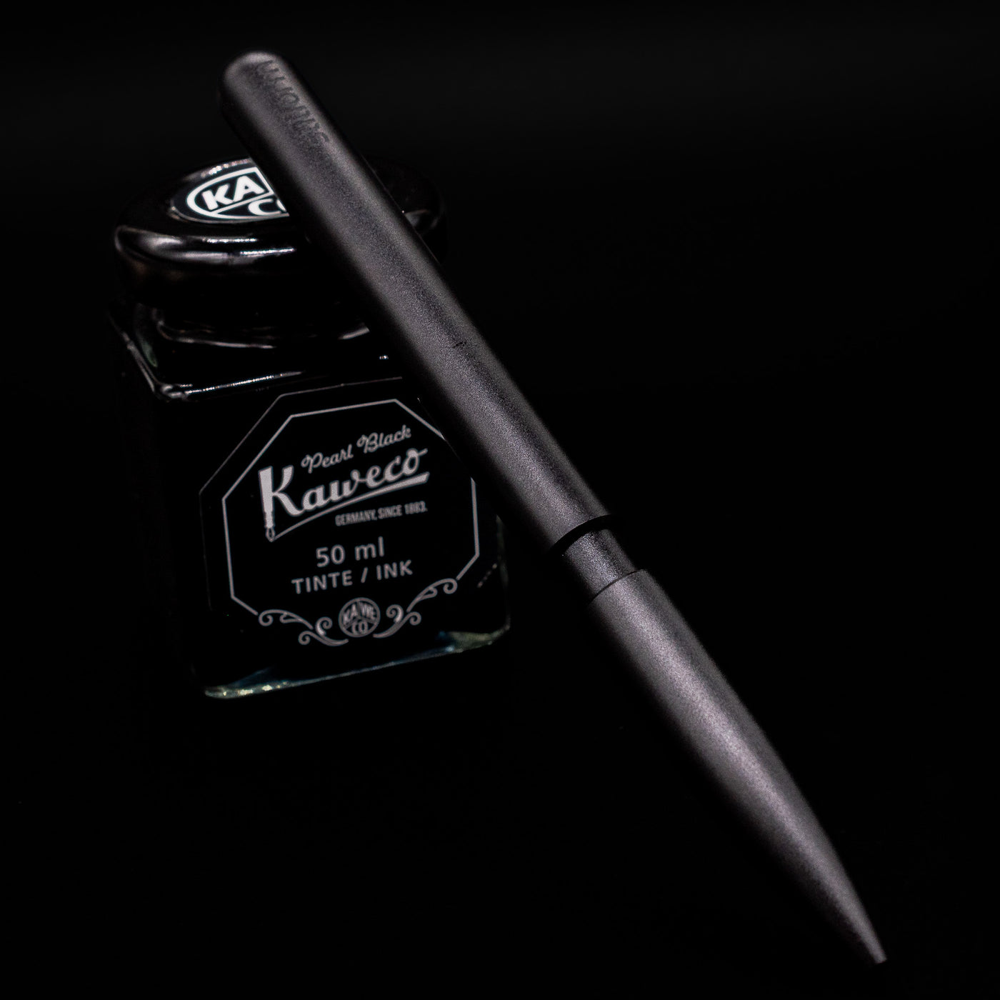 Stilform PEN Ballpoint Pen – Warp Black Aluminum leaning on an ink bottle.