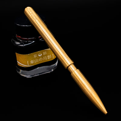 Stilform PEN Ballpoint Pen – Brass Radial Brushed leaning on an ink bottle.