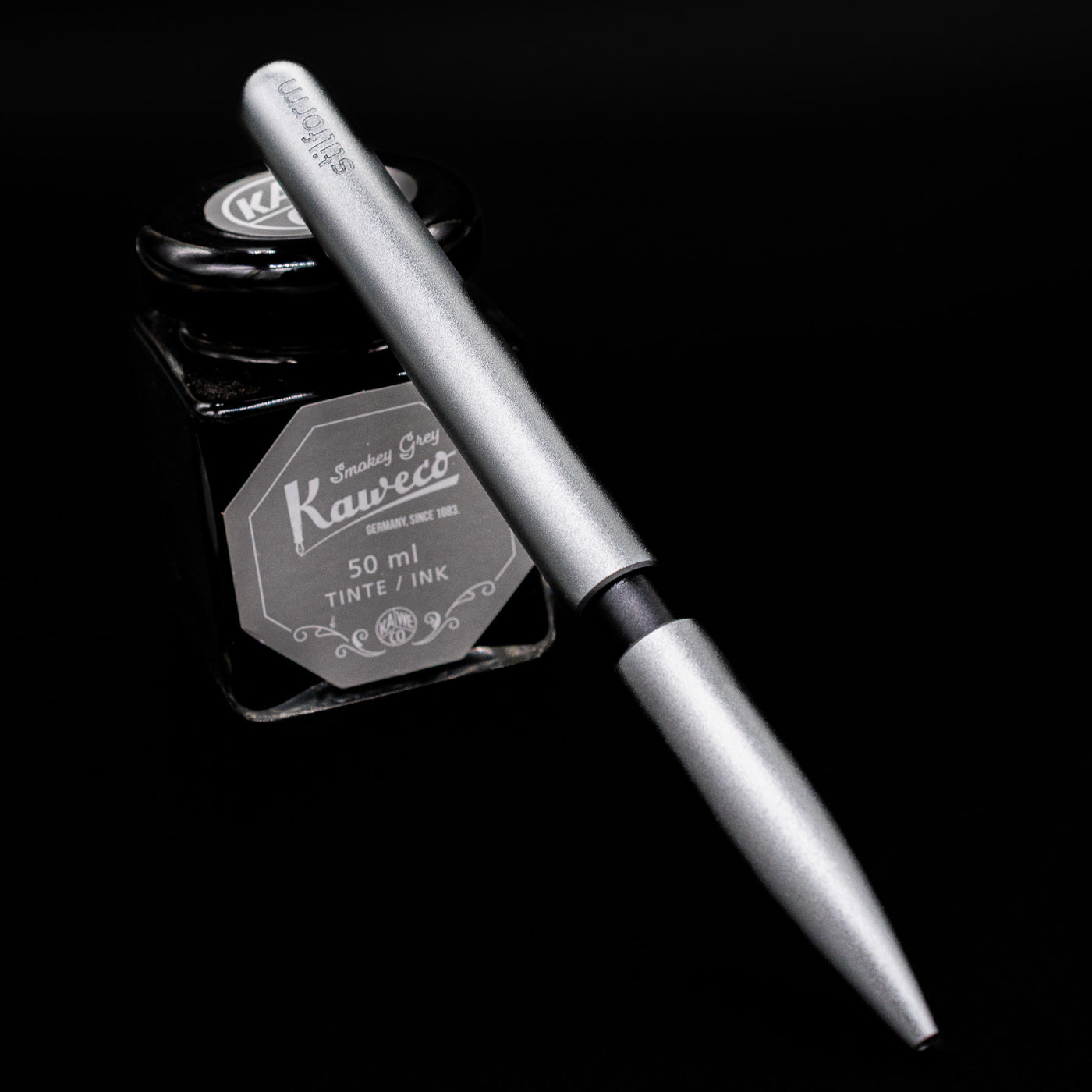 Stilform PEN Ballpoint Pen – Comet Grey Aluminum leaning on an ink bottle.