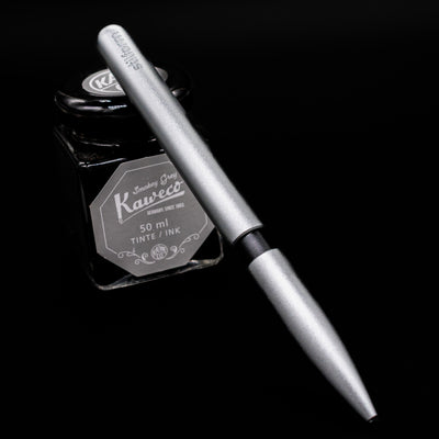 Stilform PEN Ballpoint Pen – Comet Grey Aluminum leaning on an ink bottle.