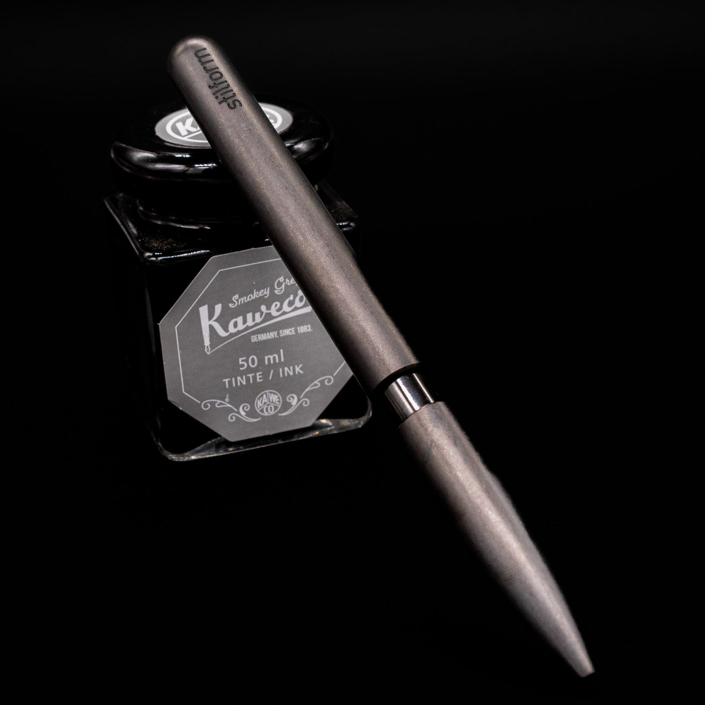 Stilform PEN Ballpoint Pen – Titanium DLC leaning on an ink bottle.