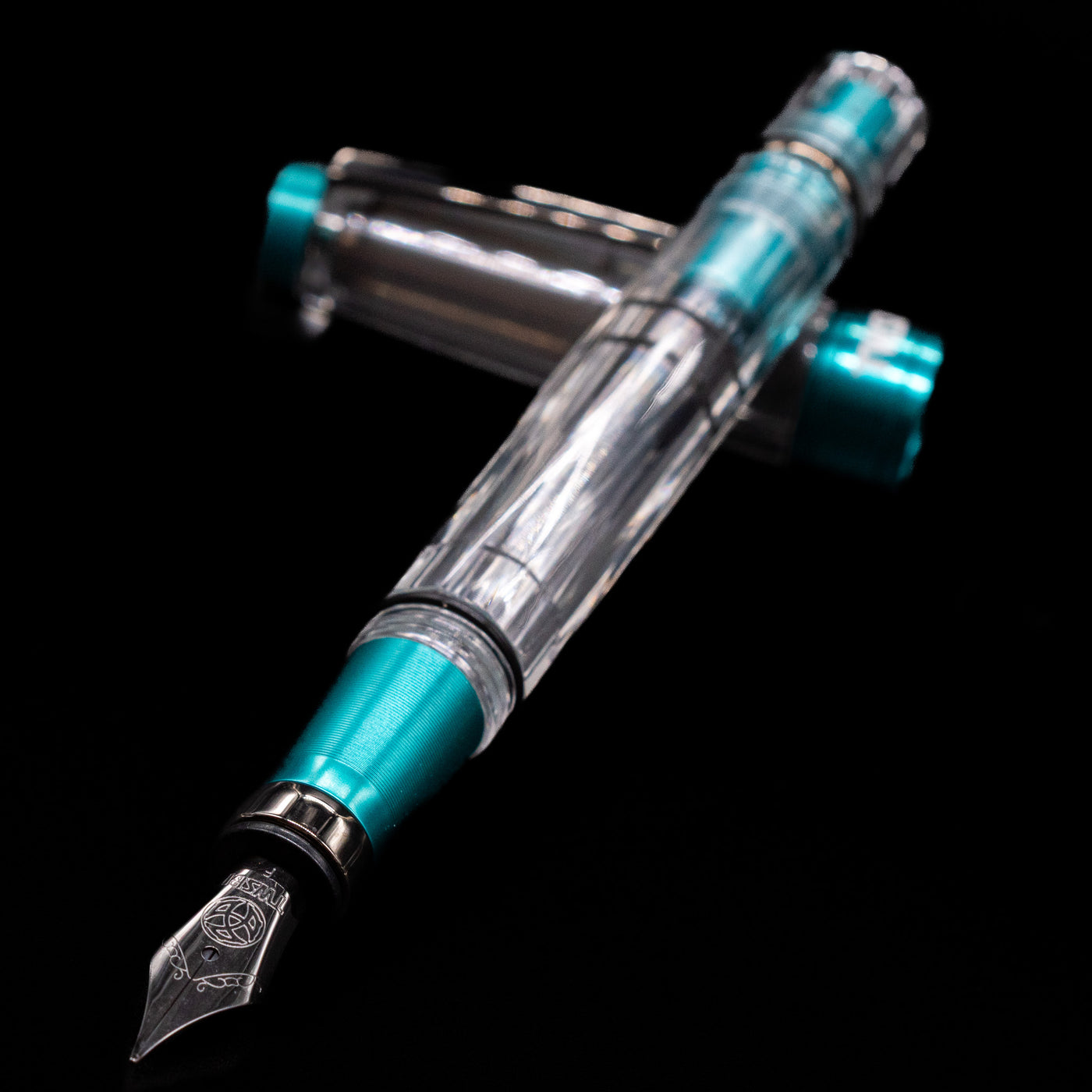 TWSBI Diamond 580 Caribbean Blue & Onyx Fountain Pen - Preowned laying across its own cap, crossed, with a focus on the nib.