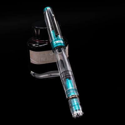 TWSBI Diamond 580 Caribbean Blue & Onyx Fountain Pen - Preowned capped, leaning against an ink bottle. 