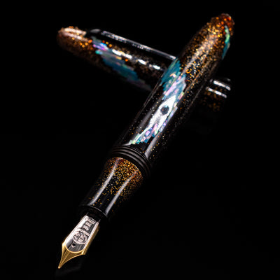 Taccia Miyabi Bon Bori Aurora Glimmer Fountain Pen laying across its own cap, crossed, with a focus on the nib.