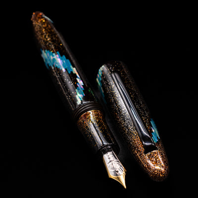 A full view of the Taccia Miyabi Bon Bori Aurora Glimmer Fountain Pen uncapped, with its cap laying next to the pen. 