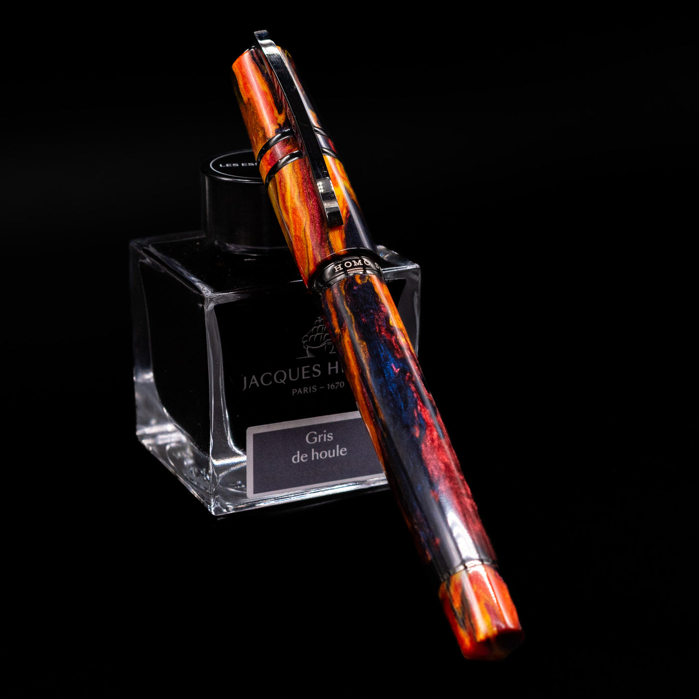 Visconti Homo Sapiens Earth Origins Fire edition fountain pen capped, leaning against an ink bottle, showing its fiery red-orange marbled resin with a metal trim.