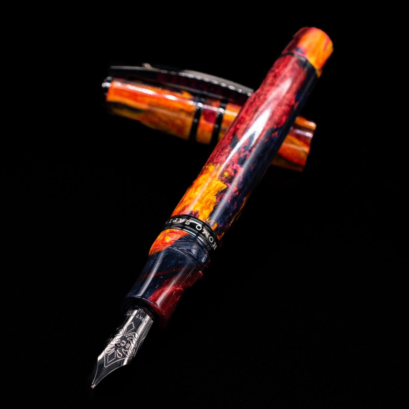Pen and cap crossed, nib sharply focused, glowing marbled resin background on the Visconti Homo Sapiens Earth Origins Fire edition fountain pen.