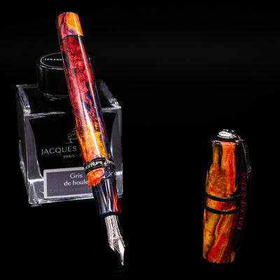 Visconti Homo Sapiens Earth Origins Fire edition fountain pen uncapped, nib revealed, resting on an ink bottle, highlighting the lava-inspired marbled body.
