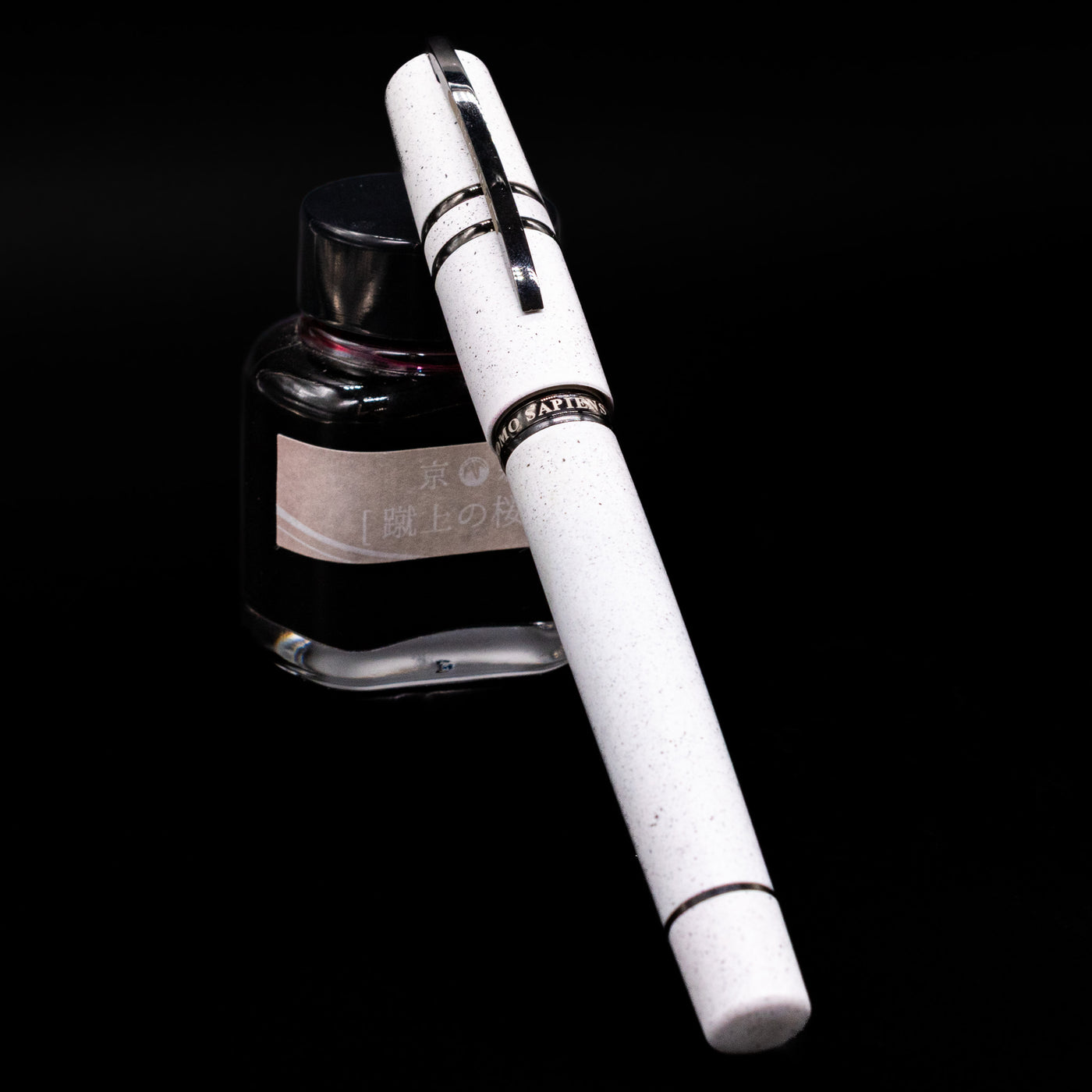 Visconti Homo Sapiens Fountain Pen - Blizzard White capped, leaning against an ink bottle. 
