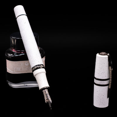 Visconti Homo Sapiens Fountain Pen - Blizzard White leaning on an ink bottle uncapped showcasing the detailing on the nib.