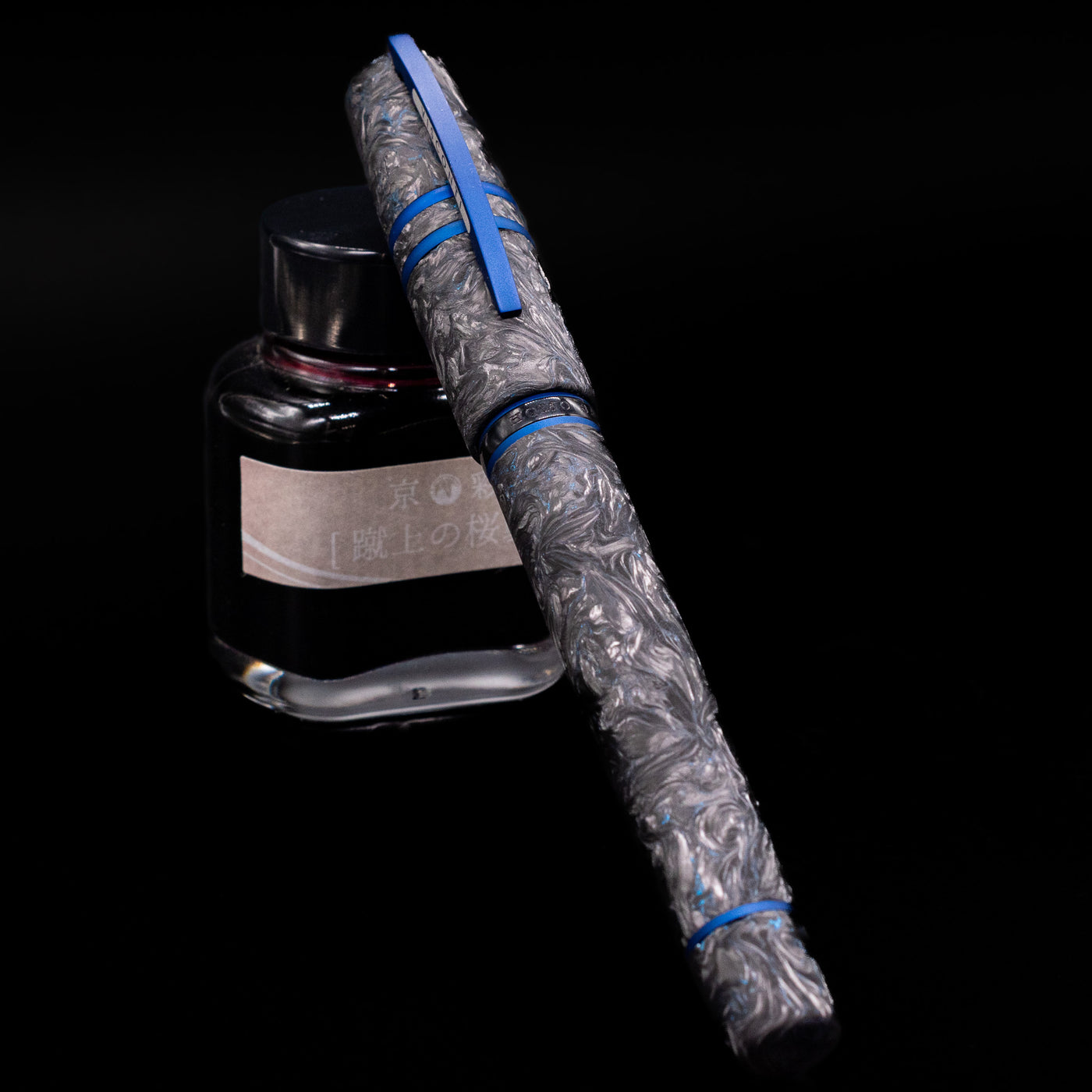 Visconti Homo Sapiens Fountain Pen - Carbon Abyssus capped, leaning against an ink bottle. 