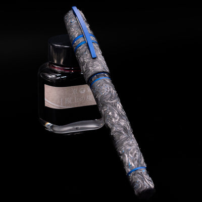 Visconti Homo Sapiens Fountain Pen - Carbon Abyssus capped, leaning against an ink bottle. 