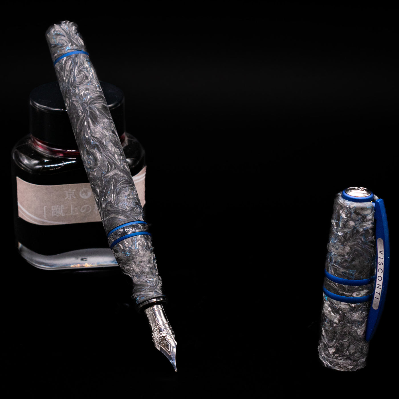 Visconti Homo Sapiens Fountain Pen - Carbon Abyssus leaning on an ink bottle uncapped showcasing the detailing on the nib.