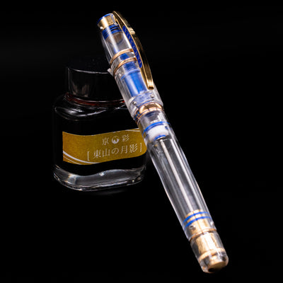 A transparent Visconti Homo Sapiens Full Demo fountain pen, capped, resting diagonally against an ink bottle.