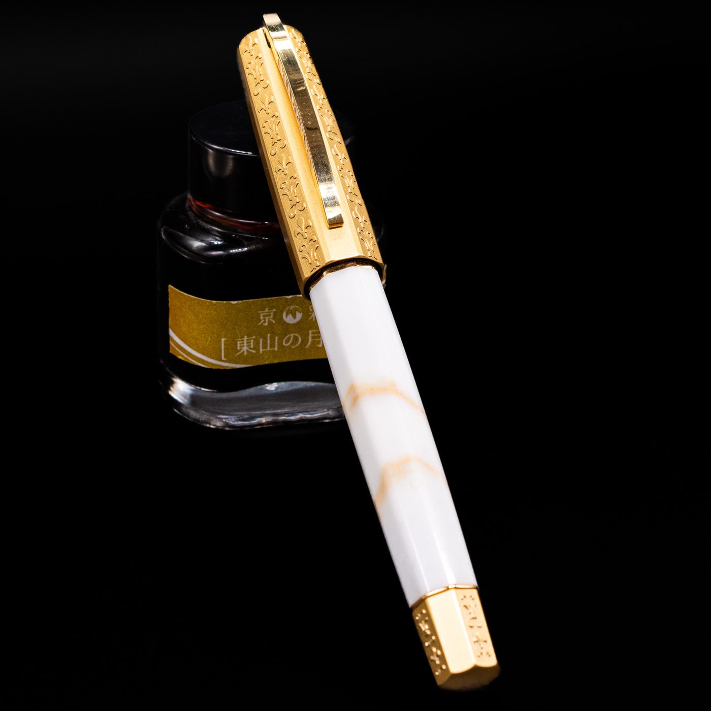 Visconti Il Magnifico Calacatta Gold Fountain Pen capped, leaning against an ink bottle. 