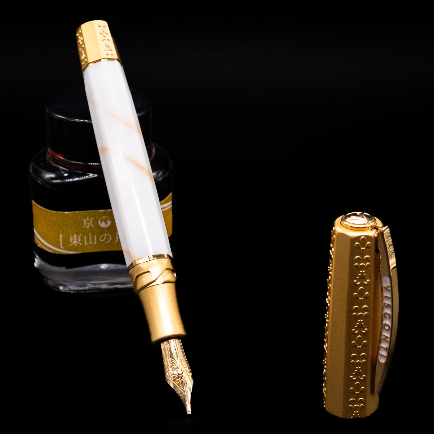 Visconti Il Magnifico Calacatta Gold Fountain Pen leaning on an ink bottle uncapped showcasing the detailing on the nib.