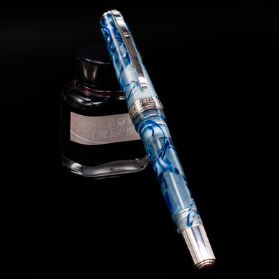 Visconti Manhattan Fountain Pen - Ice Blue capped, leaning against an ink bottle. 
