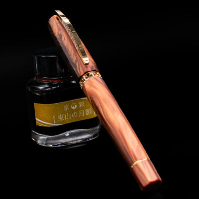 Visconti Medici Briarwood Fountain Pen in Gold capped, leaning on an ink bottle.